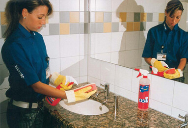 Frau reinigt Waschbecken mit Schwamm und Spray im Sanitärraum.